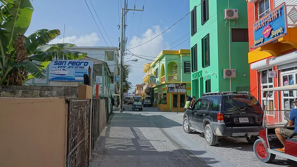 Barrier Reef Street in San Pedro, with painted timber and concrete shopfronts either side, overhead power lines, a parked SUV and a golf cart.