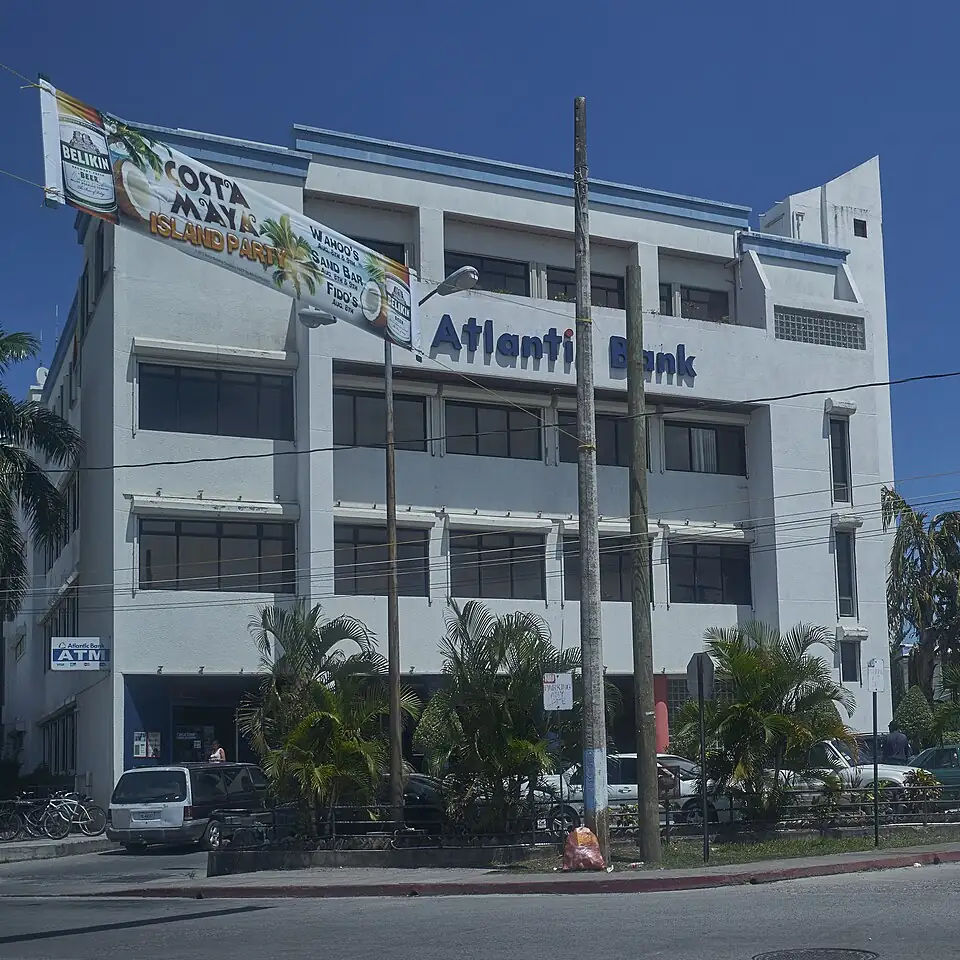 A three-storey white building lettered Atlantic Bank across its upper facade, with an Atlantic Bank ATM sign beside the ground-floor entrance and palms and parked cars in front.