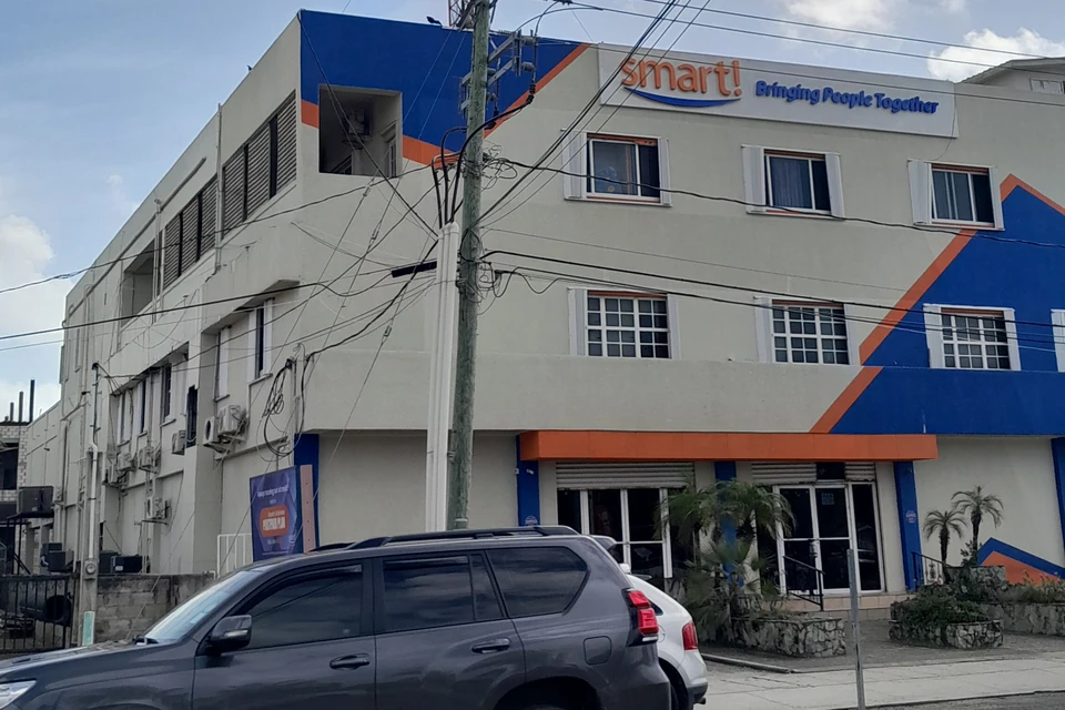 A three-storey building painted blue, orange and cream with a 'smart! Bringing People Together' sign across its upper front and a telecom mast on the roof.