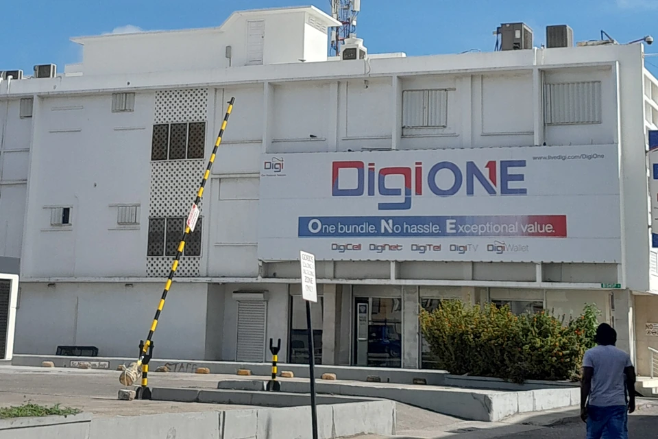 A white building on a street corner carrying a large DigiONE billboard listing DigiCell, DigiNet, DigiTel, DigiTV and DigiWallet, with a telecom mast on the roof and a shopfront below.