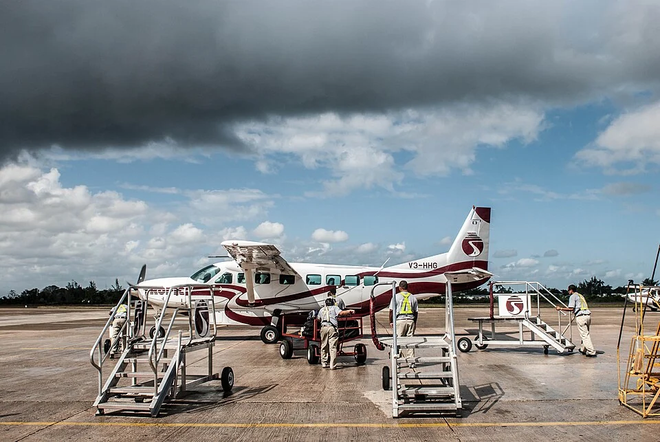 A Tropic Air Cessna Caravan being loaded on the apron at Belize's international airport, with boarding stairs and ground crew alongside it.