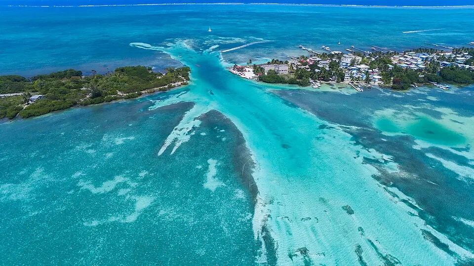 An aerial view of the channel cutting across Caye Caulker, with the village's piers and buildings lining the shore on the right.