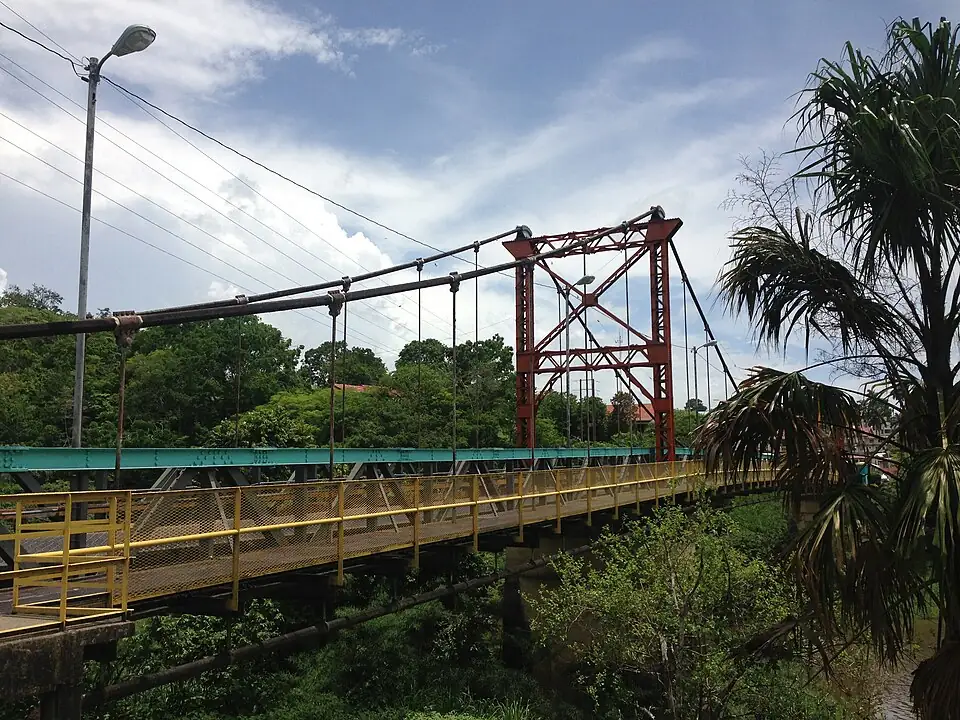 The Hawkesworth suspension bridge over the Macal River at San Ignacio, with a yellow pedestrian walkway alongside the roadway.