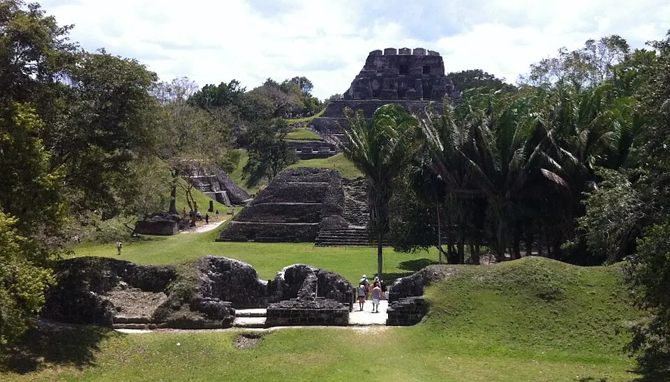 El Castillo rising above the plazas at Xunantunich, with visitors walking on the grass between lower stone structures.