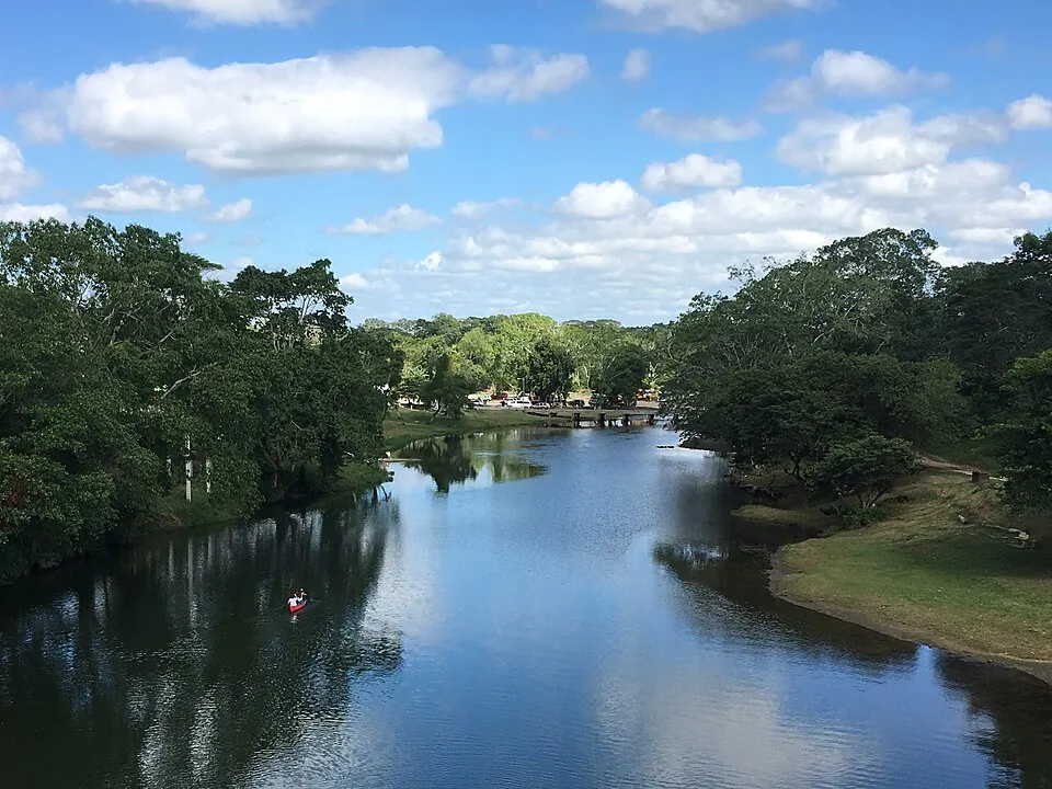 The Macal River seen from the Hawksworth Bridge at San Ignacio, with a canoe on the water and forest along both banks.