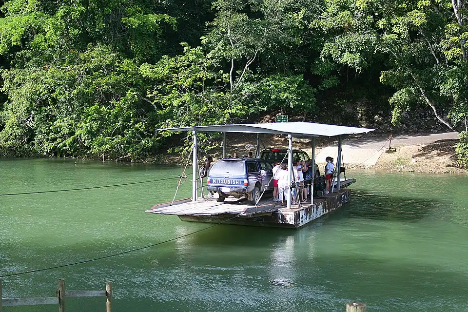 The hand-cranked cable ferry crossing the Mopan River with a four-wheel-drive vehicle aboard and passengers standing beside it.